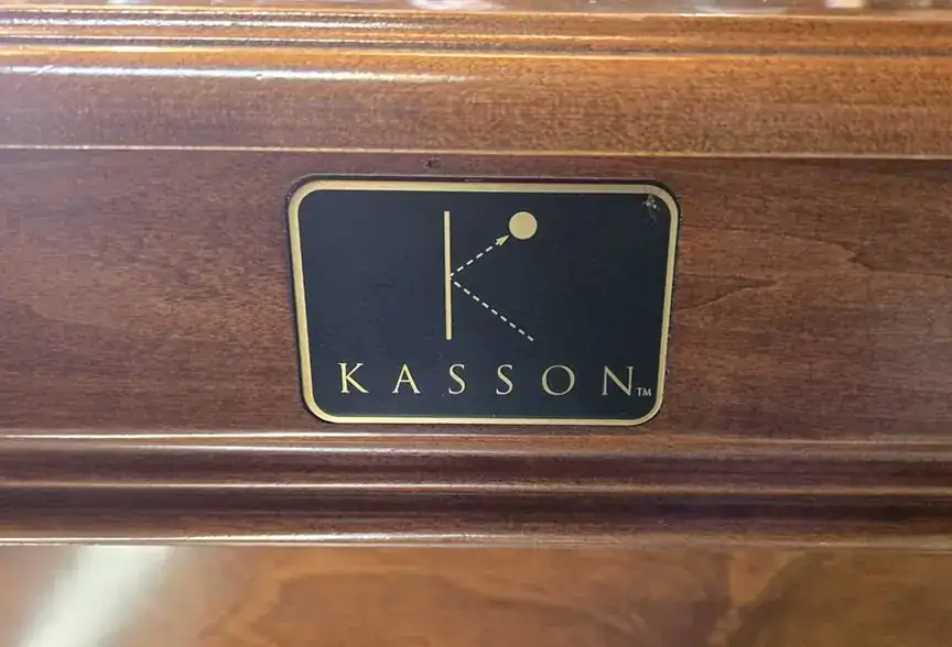 A brass-framed Kasson badge set into the wooden rail of a pool table