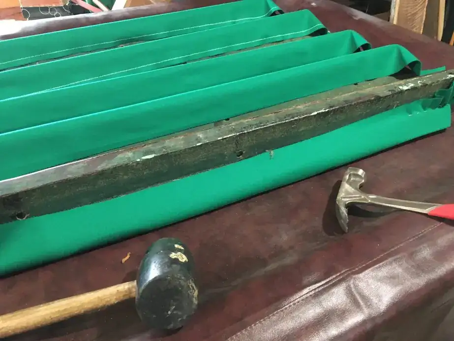 Pool table rails with green cloth lined up on a table beside a rubber mallet