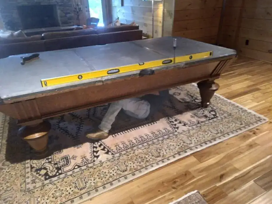 A long level laid across bare slate on a pool table frame during setup