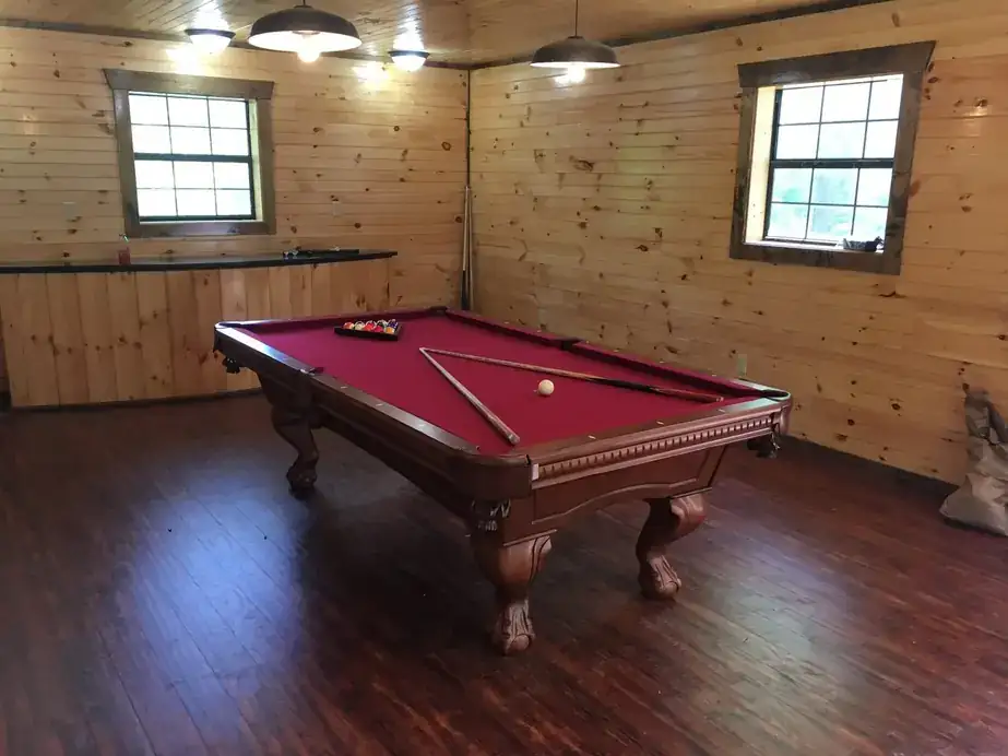 A burgundy-cloth pool table with carved legs set up in a knotty pine game room