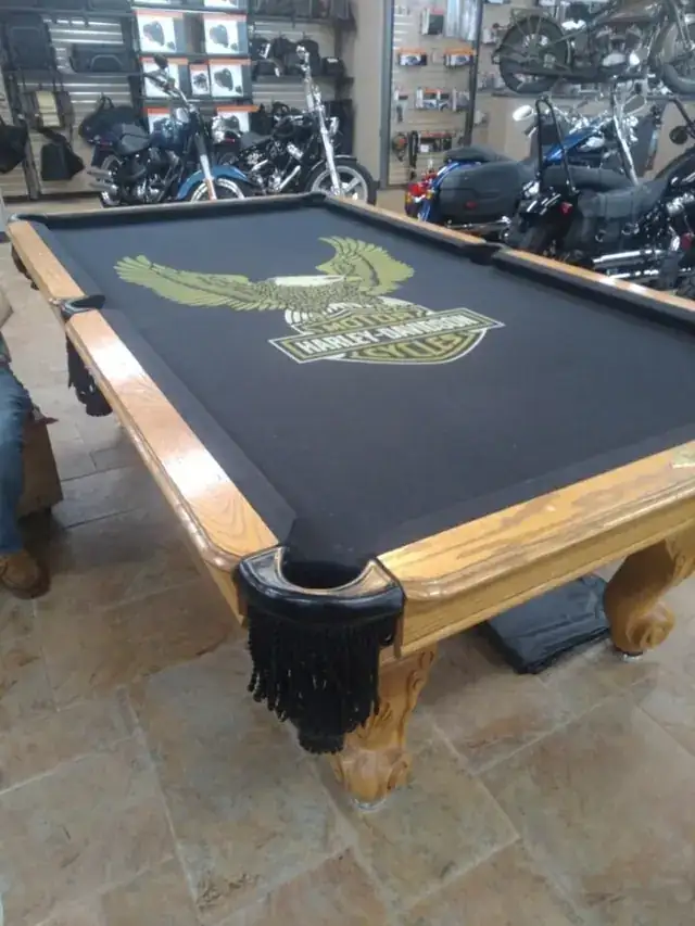 A pool table fitted with custom cloth featuring a Harley-Davidson logo