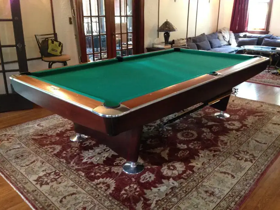 A mahogany pool table with green cloth on a red rug