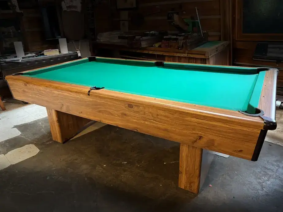 An oak pedestal pool table with green cloth in a garage