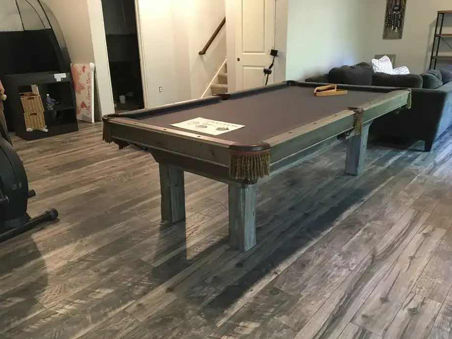 A grey-cloth pool table on a wood plank floor