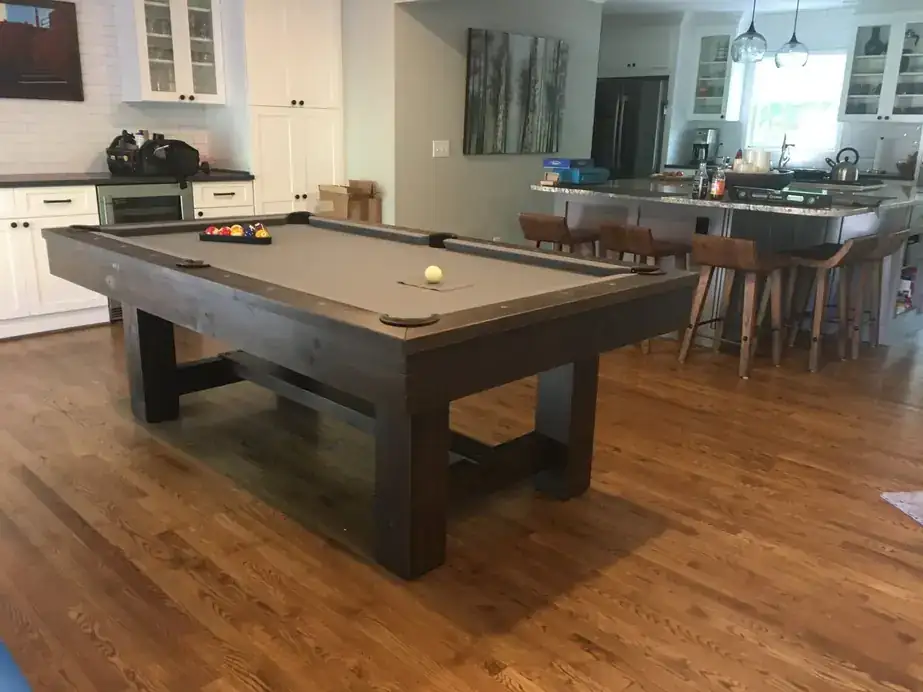 A rustic grey-cloth pool table near a kitchen