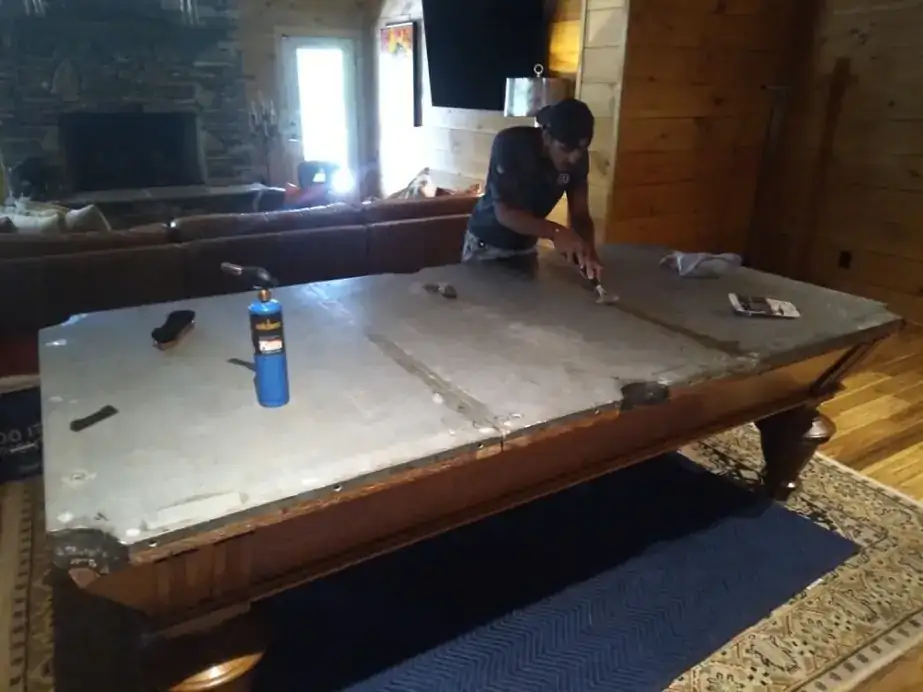 A crew member working on the slate seams of a disassembled pool table